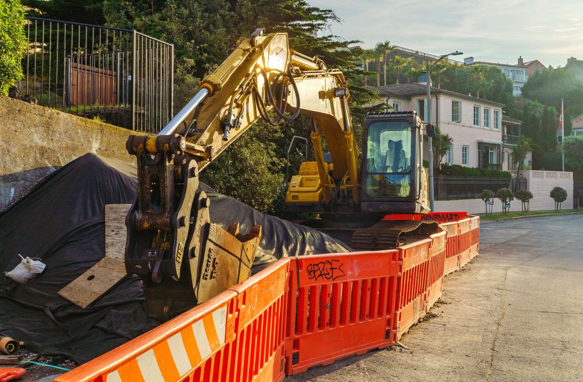 Mini excavator working on a residential street behind safety barriers