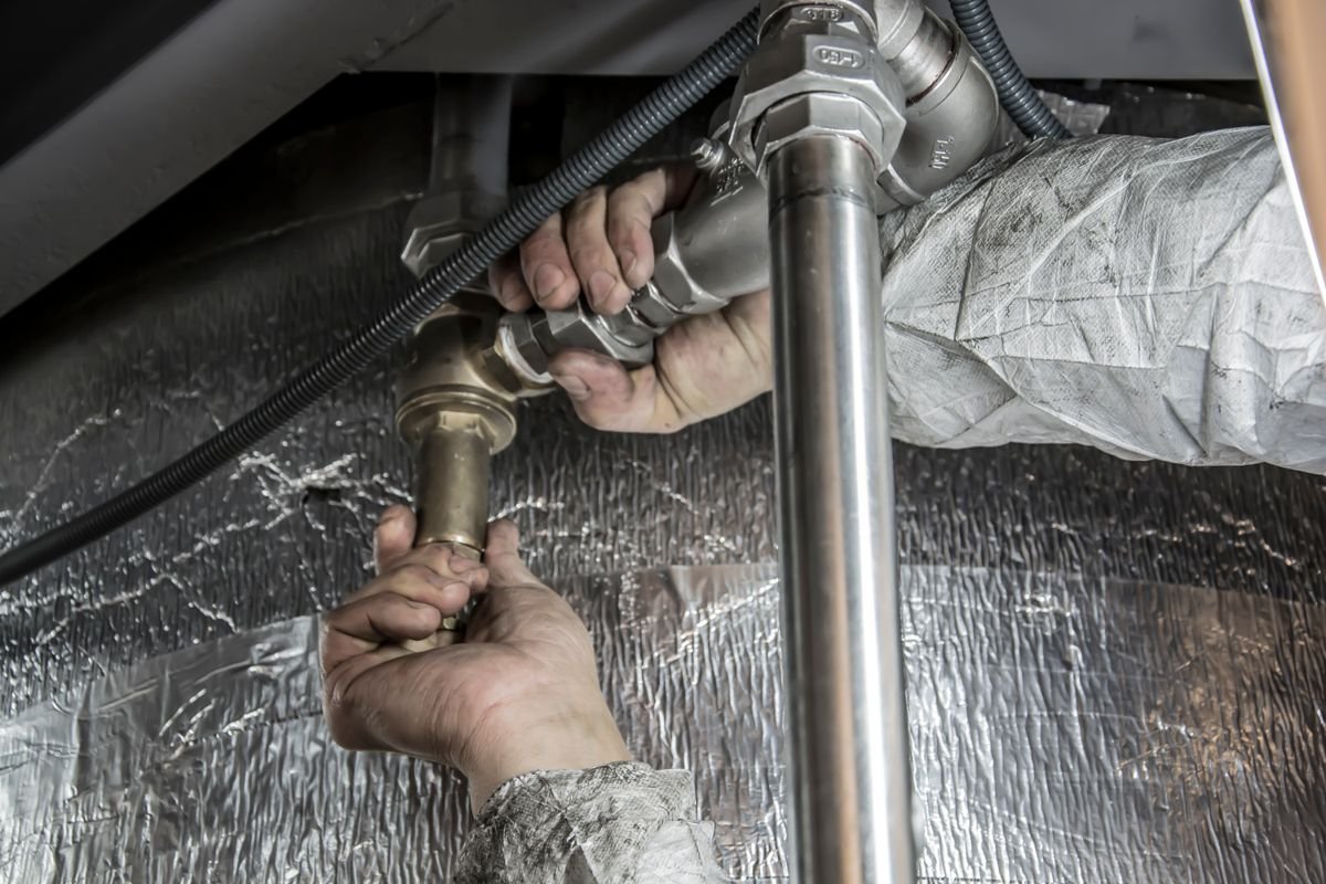 Plumber's hands fitting a valve onto a steel pipe