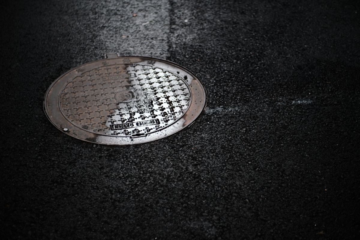 Sewer manhole cover set into wet asphalt pavement